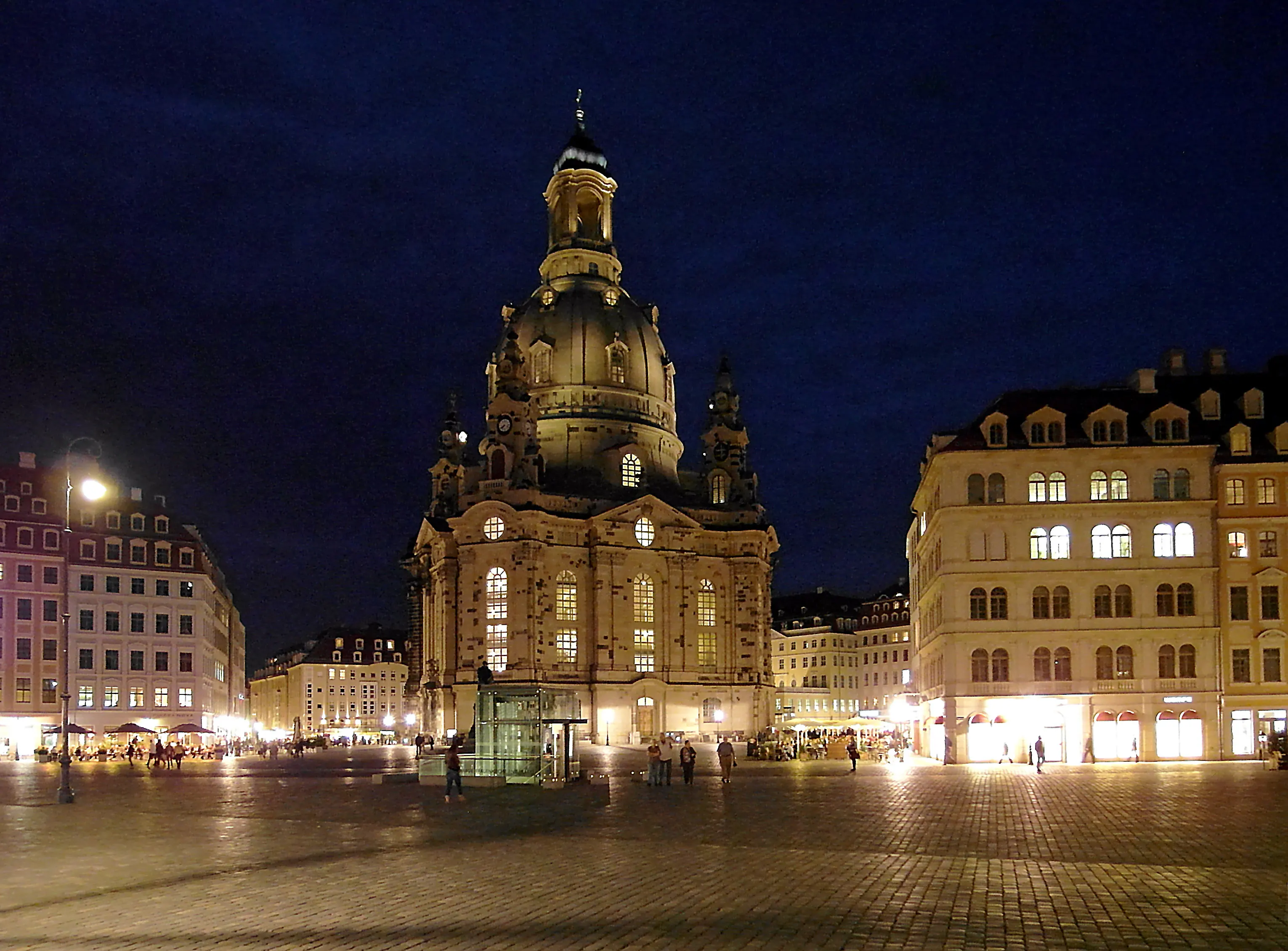 Die Frauenkirche zu Dresden bei Nacht auf dem Neumarkt, ihre barocke Sandsteinkuppel warm angestrahlt vor tiefblauem Himmel.