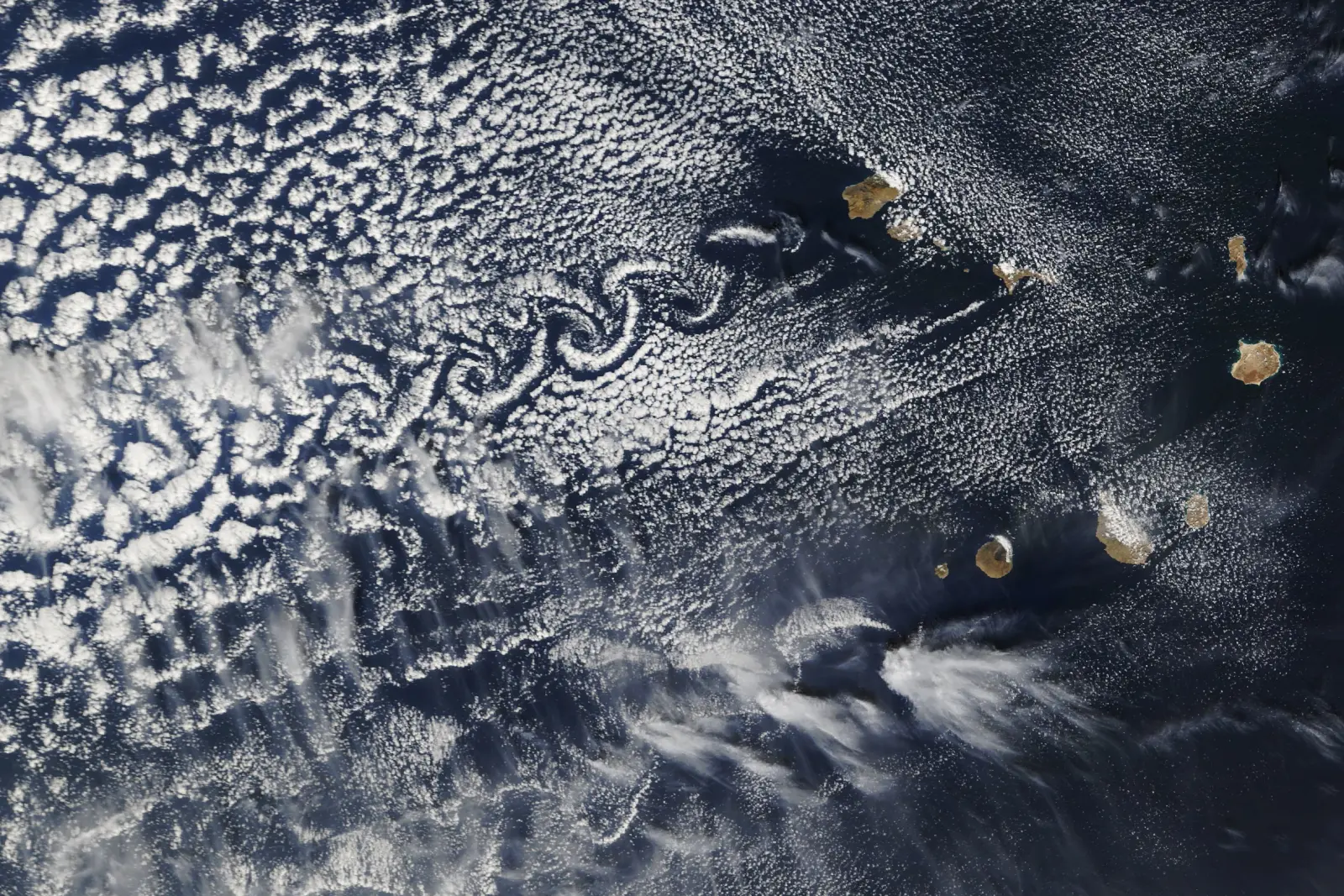 NASA-Satellitenbild der Kapverdischen Inseln: hinter den Vulkangipfeln von Fogo, Santo Antão und São Nicolau wirbeln gestaffelte, gegenläufige Wolken-Spiralen über den Atlantik — eine Von-Kármán-Wirbelstraße.