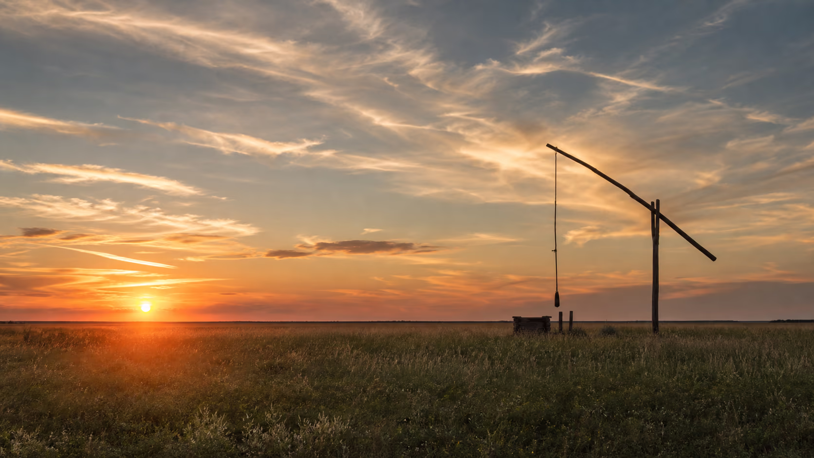 Weite, flache Puszta-Ebene im warmen Gegenlicht des Sonnenuntergangs, dunstiger Horizont — Lebensraum für Wasserbüffel und Nonius-Pferde.