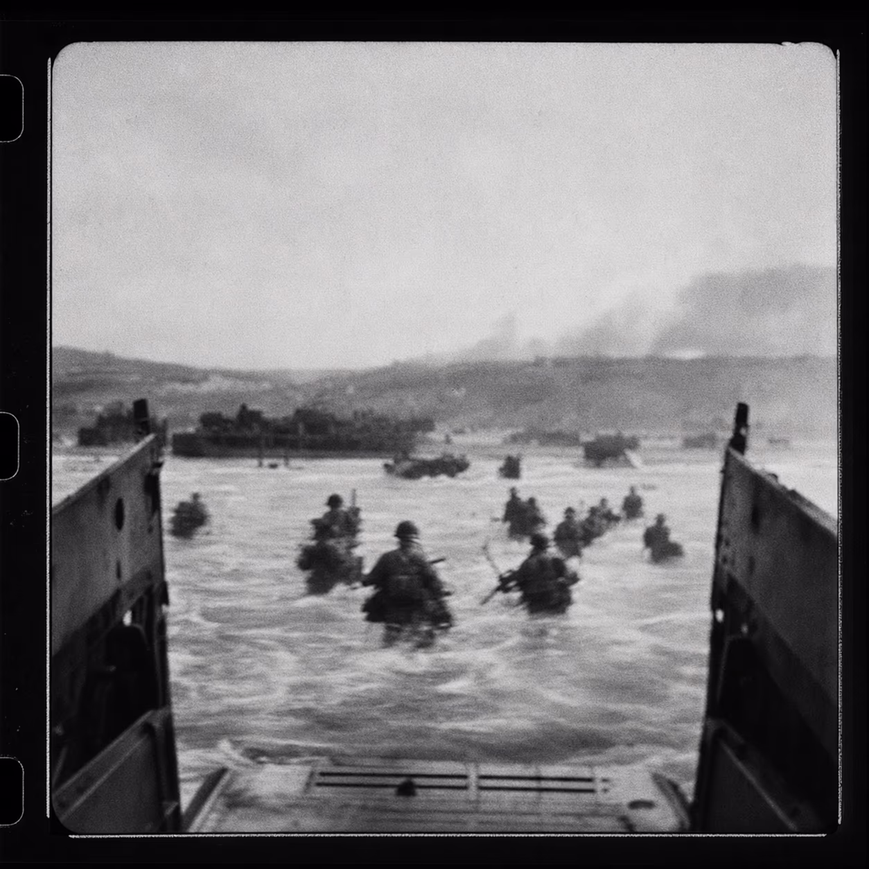 Illustration im Kontaktbogen-Stil — körnige, unscharfe Strand-/Landungs-Andeutung in Schwarz-Weiß. Keine Aufnahme von Robert Capa; KI-Illustration.