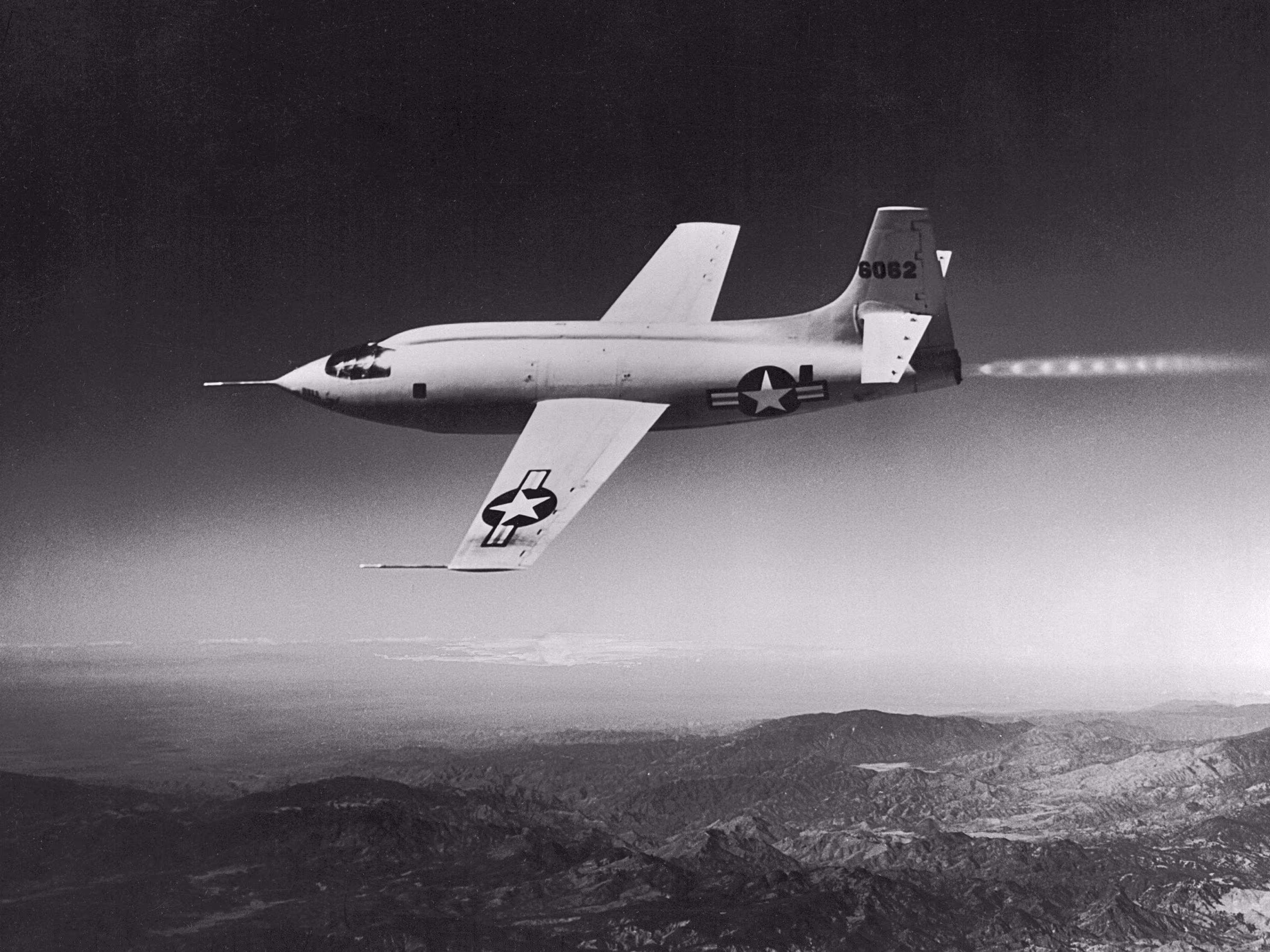 Die Bell X-1 (Kennung 46-062) im Flug — ein orangefarbenes, geschossförmiges Raketenflugzeug mit kurzen geraden Tragflächen.