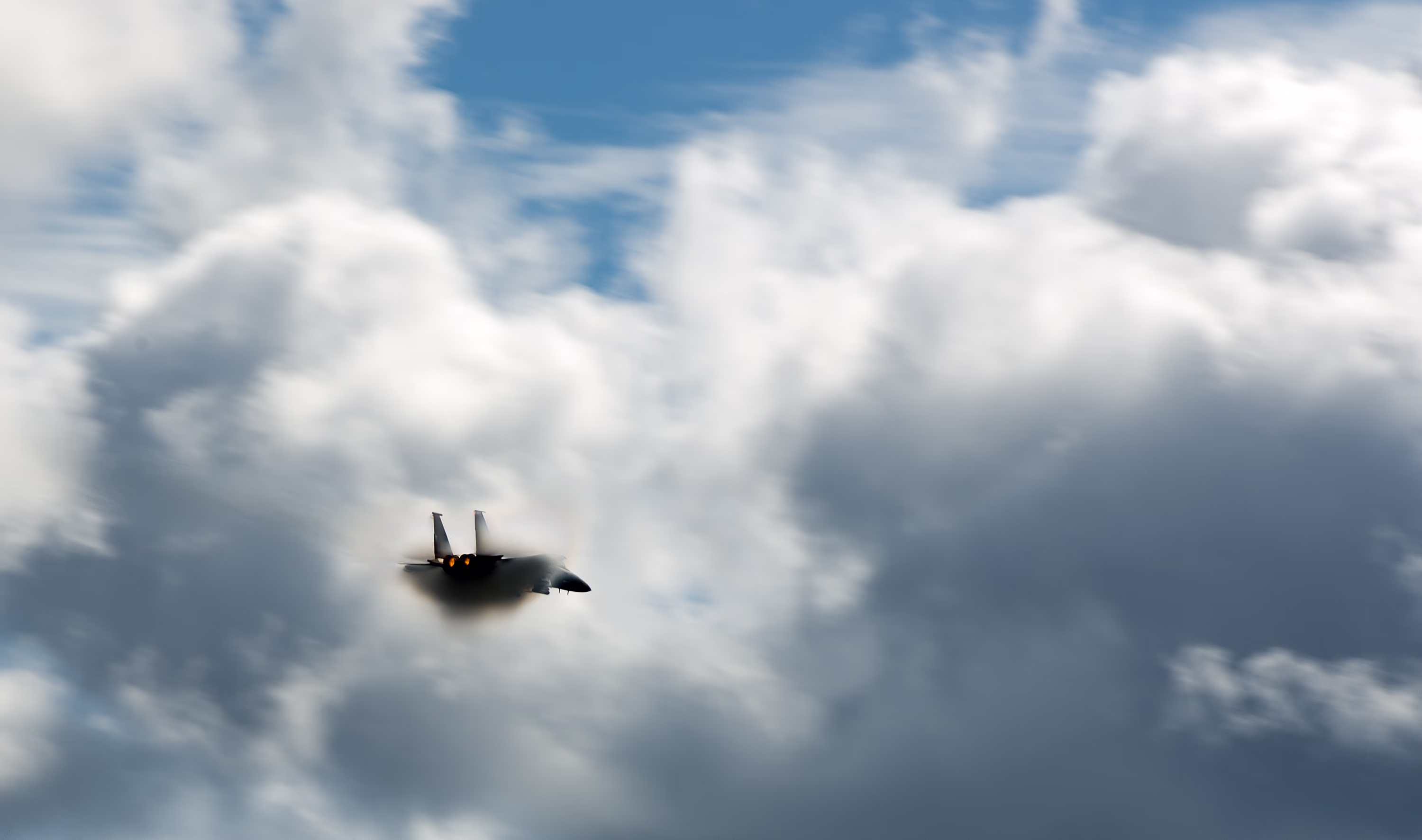 Ein Kampfjet umhüllt von einer weißen, kegelförmigen Kondensationswolke (Vapor Cone) im transsonischen Flug.